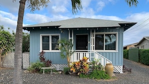 A small, single-story house with a porch, surrounded by a gravel driveway and a white picket fence.