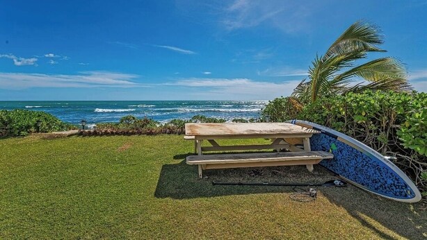 A picnic table by the ocean with a surfboard leaning against it.