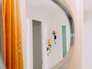 Un couloir avec une porte, un porte-bougie fixé au mur et un miroir qui reflète une partie de la pièce.