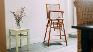 A room with a wooden chair, a small table, and a vase with dried flowers.