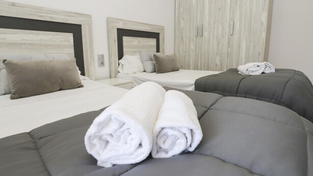 Une chambre d’hôtel moderne avec deux lits, une literie aux tons de gris et de blanc, et une grande armoire.