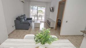 Un salon moderne avec un canapé gris, une table basse et un coin repas comprenant une table blanche et une plante en pot.