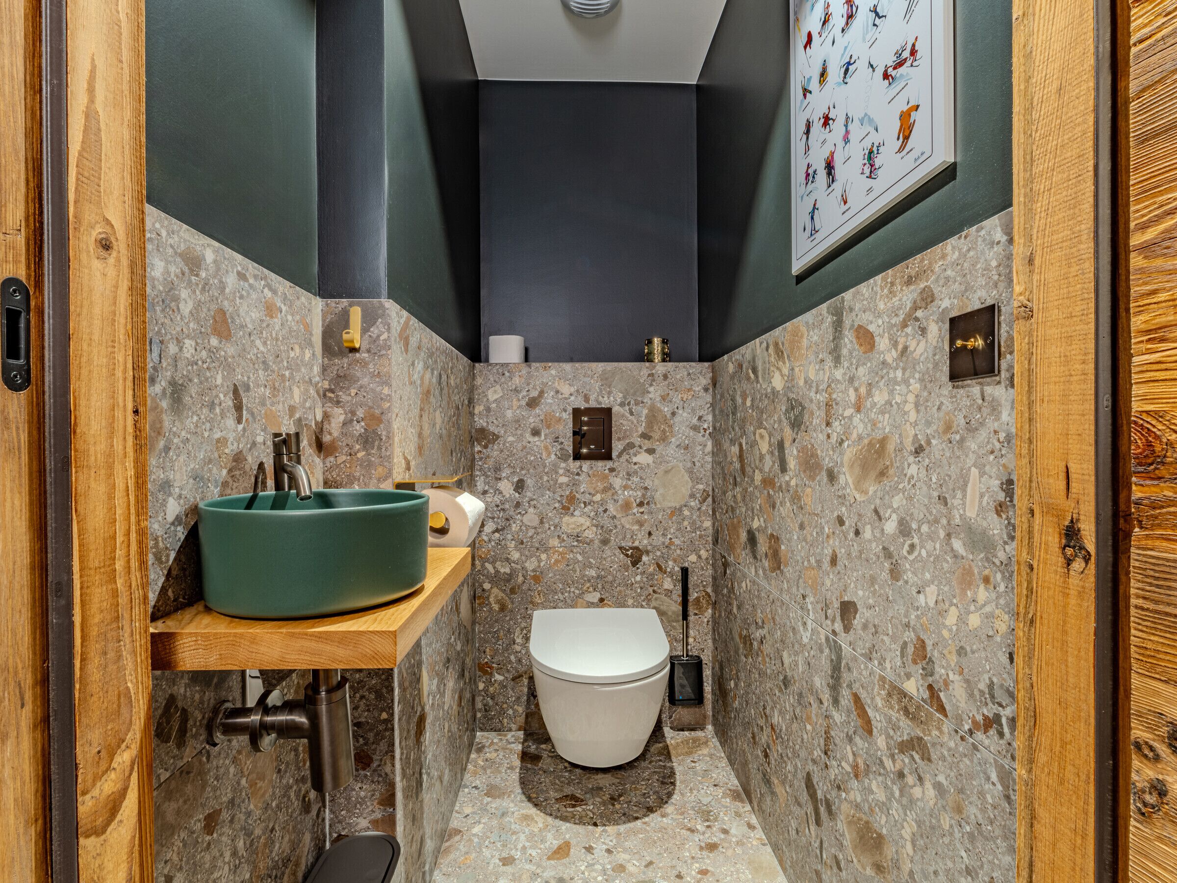 A compact bathroom with a green sink, white toilet, and a stone wall design.