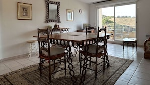 Un coin repas avec une table et des chaises en bois, un miroir décoratif et une vue sur un balcon, accessible par une grande porte-fenêtre coulissante.