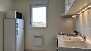 Une cuisine compacte équipée d’un réfrigérateur, d’une fenêtre donnant sur la campagne, d’un évier encastré et d’un système de ventilation.
