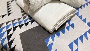 A bed with a patterned bedspread and two rolled white towels. - Pousada santos  (Barreirinhas)