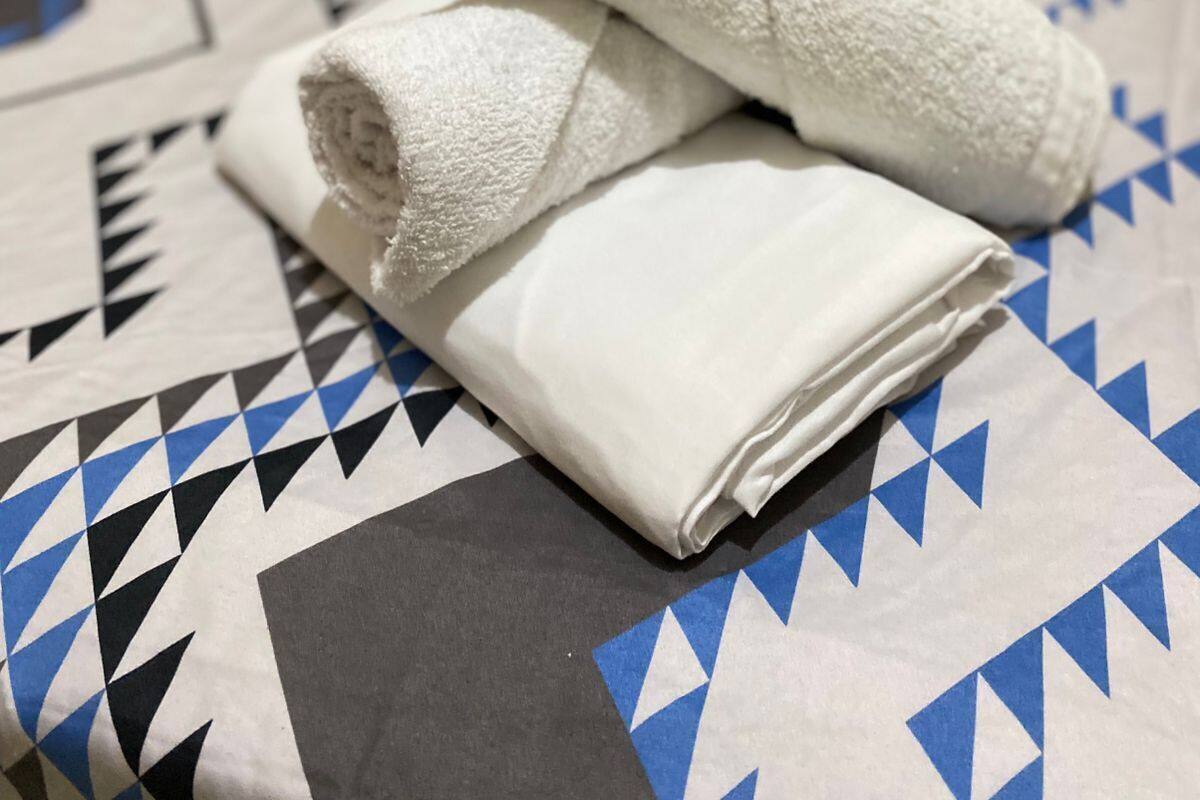 A bed with a patterned bedspread and two rolled white towels.