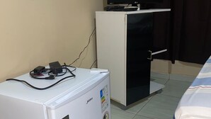 A compact room with a white mini-fridge, a small black TV on a white cabinet, and a striped bedspread. - Pousada santos  (Barreirinhas)