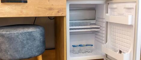Una kitchenette compacta con refrigerador incorporado, una encimera de madera y un taburete.