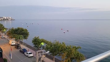 Un paisaje urbano costero con mar tranquilo, edificios y coches aparcados a lo largo del paseo marítimo.