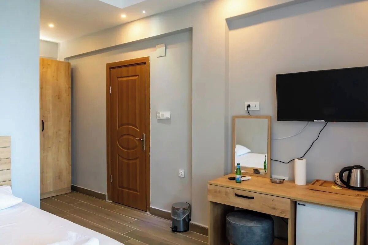 Ein Hotelzimmer mit Holztür, einem flachbildfernseher an der Wand, einem Holztisch mit Spiegel und einem Mülleimer.