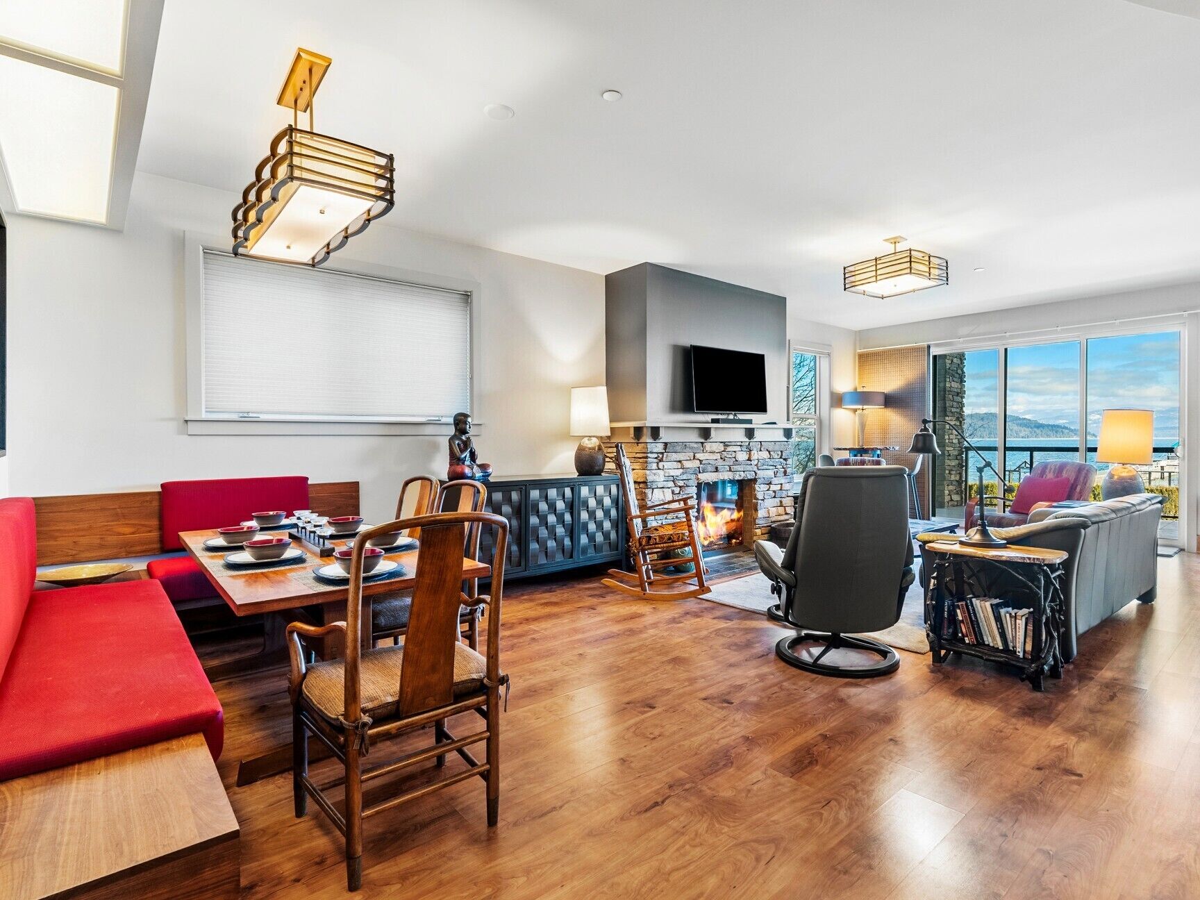 Un salon moderne doté d’une cheminée, un coin repas avec des meubles en bois et un espace détente offrant une vue sur l’extérieur.
