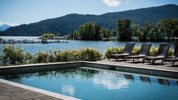 A clear swimming pool with lounge chairs and a view of a lake and forested hills. - Kids Love Hidden Bunk Room - Seasons at Sandpoint (Sandpoint)