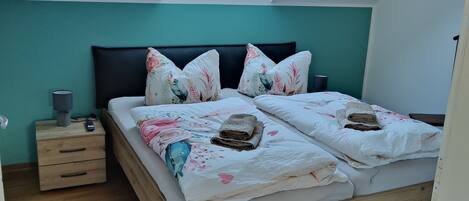 A bedroom with a skylight, a bed with floral bedding, a nightstand, and a wooden floor.