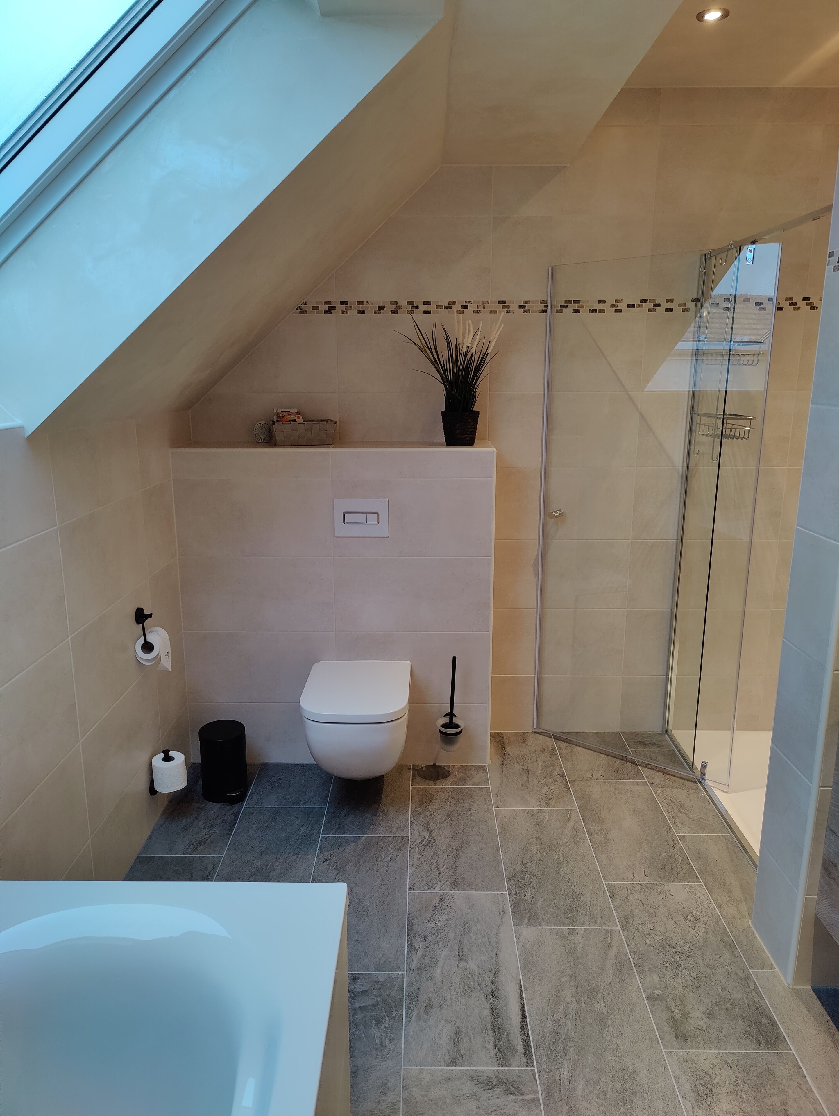 A modern bathroom with a skylight, a toilet, a shower, and a bathtub.
