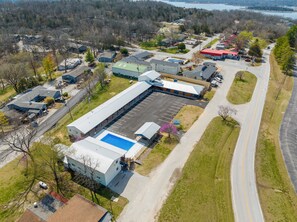 An aerial view of a large industrial building with a parking lot, surrounded by residential houses and a road.