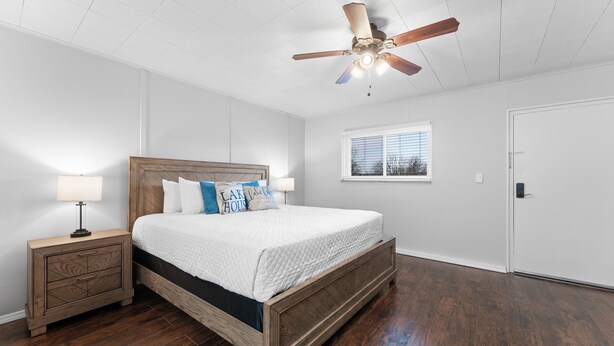 Un dormitorio con cama de madera, mesita de noche, ventilador de techo y ventana con persianas.