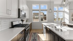 A modern kitchen with white cabinets, a stove, and a large window. - Villa #20 At Bloomington Country Club 3 Bedroom Condo (St. George)