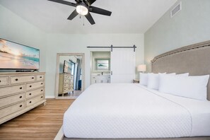 Une chambre d’hôtel avec un lit, une commode, un ventilateur de plafond, une télévision et une vue sur le couloir.