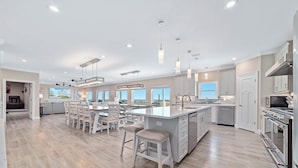 A modern kitchen with a large island, bar stools, and stainless steel appliances. - NEW Aqua Vista by GSVR | Beachfront Home w/ Pool, Theater & Game Room + Free Activities/Golf (Gulf Shores)
