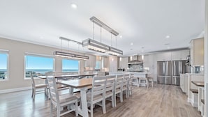 A modern kitchen with a central island, stainless steel appliances, and a view of the city. - NEW Aqua Vista by GSVR | Beachfront Home w/ Pool, Theater & Game Room + Free Activities/Golf (Gulf Shores)