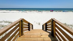 A wooden boardwalk leading to a sandy beach with umbrellas and people in the distance. - NEW Aqua Vista by GSVR | Beachfront Home w/ Pool, Theater & Game Room + Free Activities/Golf (Gulf Shores)