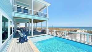 A poolside area with a view of the beach, a covered deck, and a two-story building. - NEW Aqua Vista by GSVR | Beachfront Home w/ Pool, Theater & Game Room + Free Activities/Golf (Gulf Shores)
