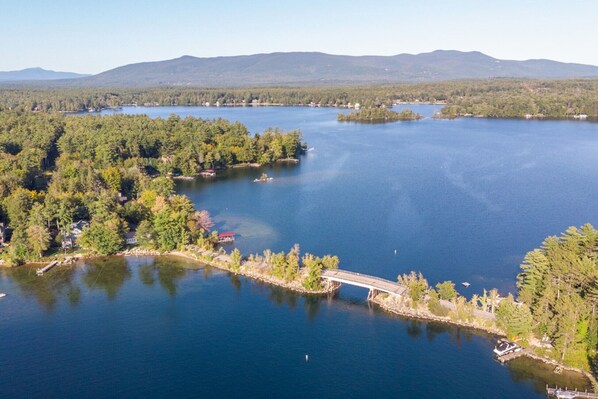 A lake surrounded by dense forest and a bridge connecting two landmasses. - Lovely Black Cat Island waterfront (Moultonborough)