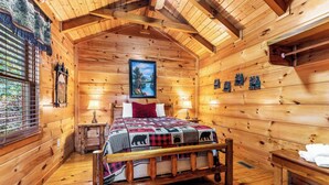 Una habitación de cabaña de madera con una cama, dos mesitas de noche, una ventana con persianas y un cuadro en la pared.