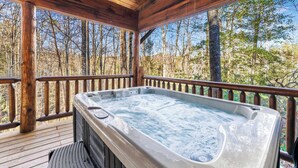 Una terraza de madera con un jacuzzi y vistas a un bosque.