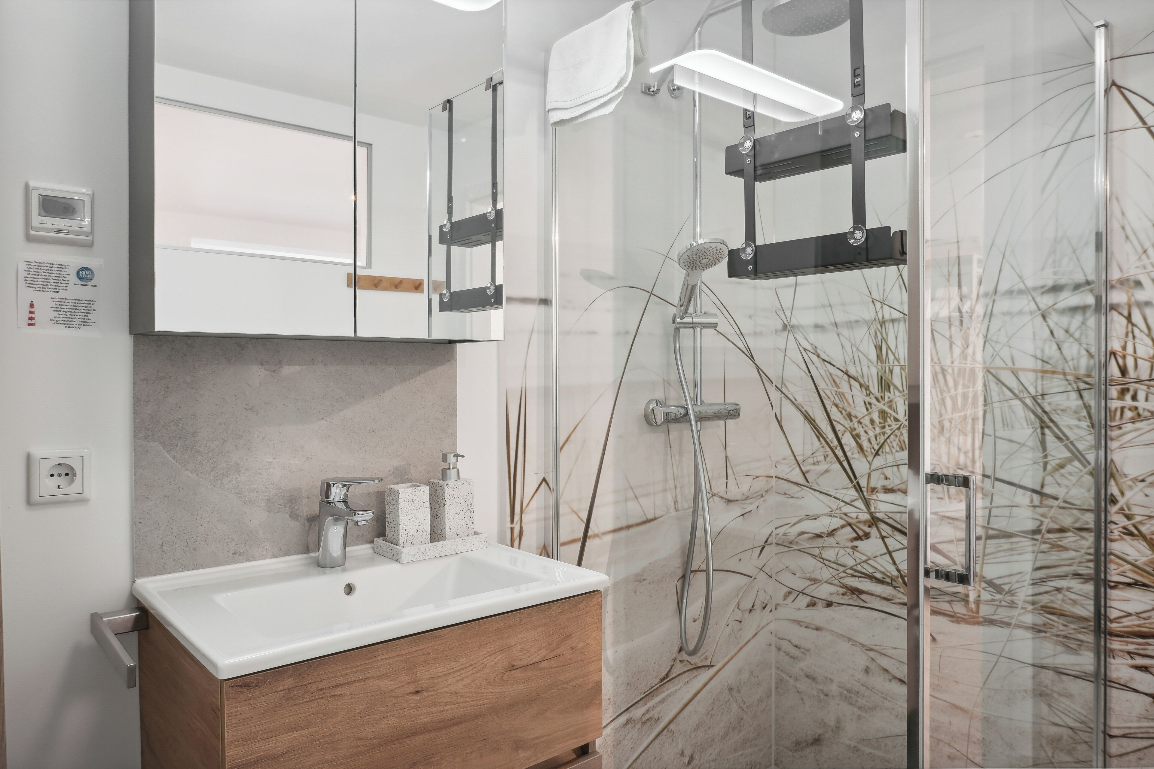Un baño moderno con lavamanos blanco, tocador de madera y cabina de ducha de vidrio.
