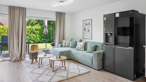 A modern living room with a sofa, a black refrigerator, and a dining area with a table and chairs. - Modern KüstenHygge 2 with garden & parking space (Westerdeichstrich)