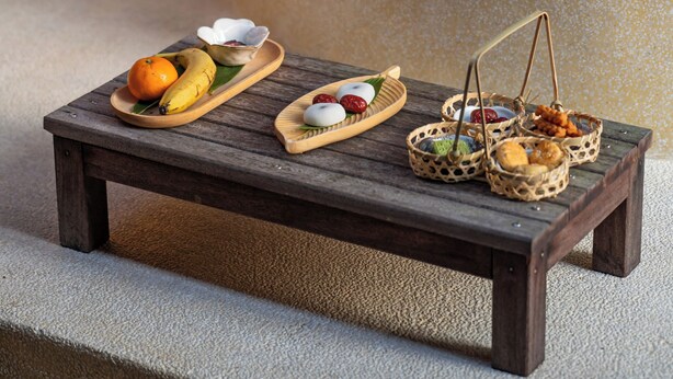 A wooden table with a variety of food items and baskets, set against a stone wall with a thatched roof in the background. - Hegu Villa Hotel (Changzhou)