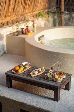 A wooden table with a variety of food items and baskets, set against a stone wall with a thatched roof in the background. - Hegu Villa Hotel (Changzhou)