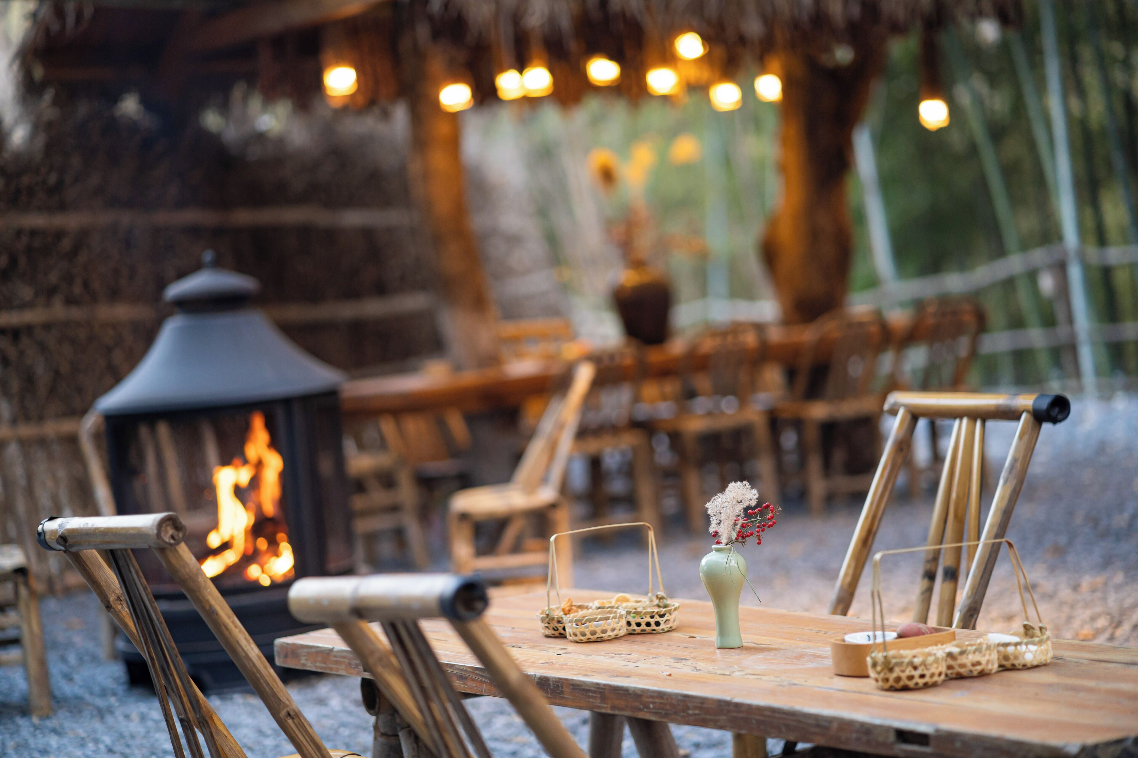 Un espacio comedor al aire libre de estilo rústico, con mobiliario de madera y una chimenea central.