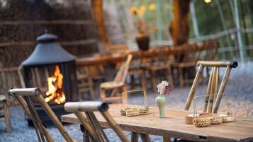 Un espacio comedor al aire libre de estilo rústico, con mobiliario de madera y una chimenea central.