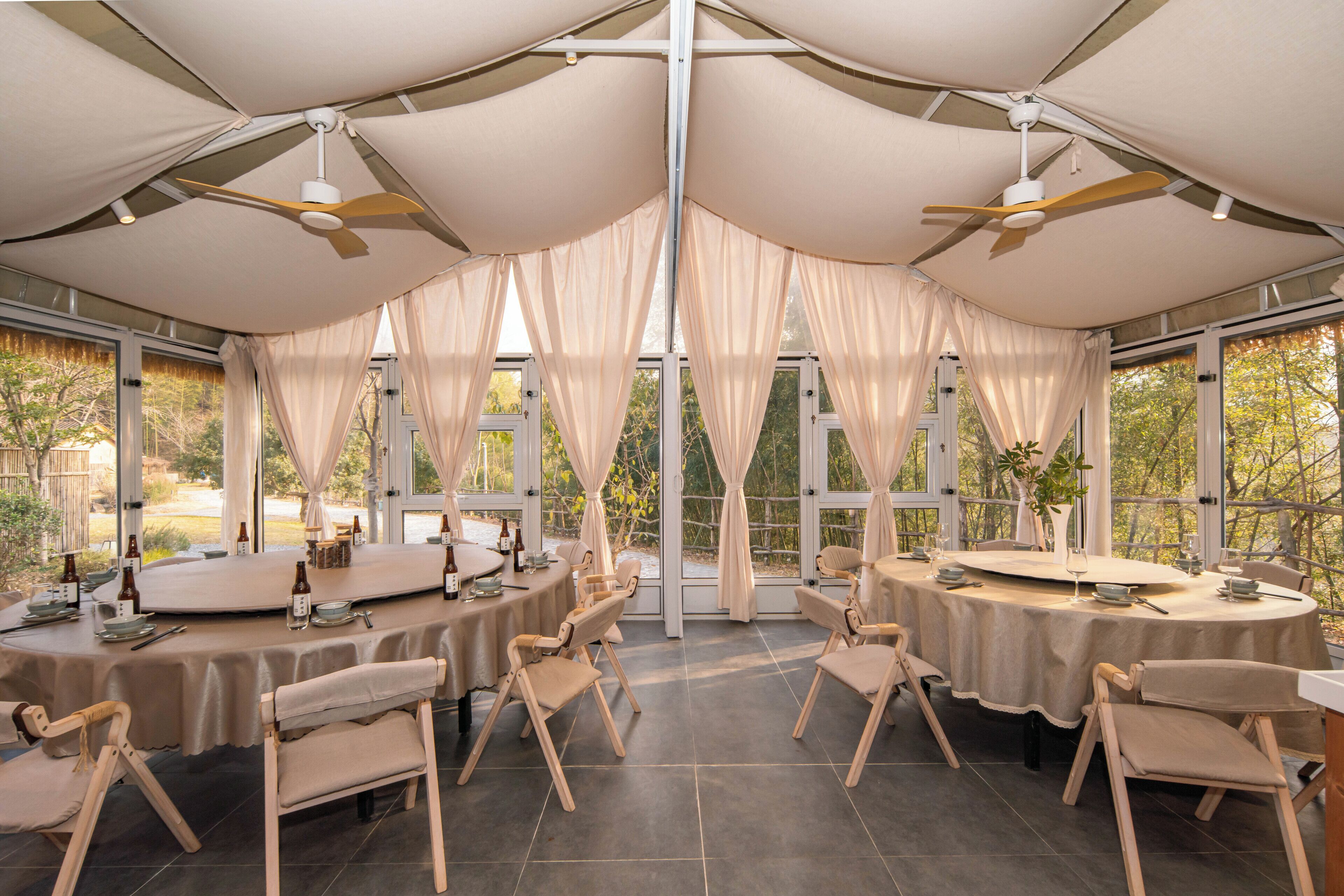 A tented dining area with round tables, chairs, and ceiling fans.