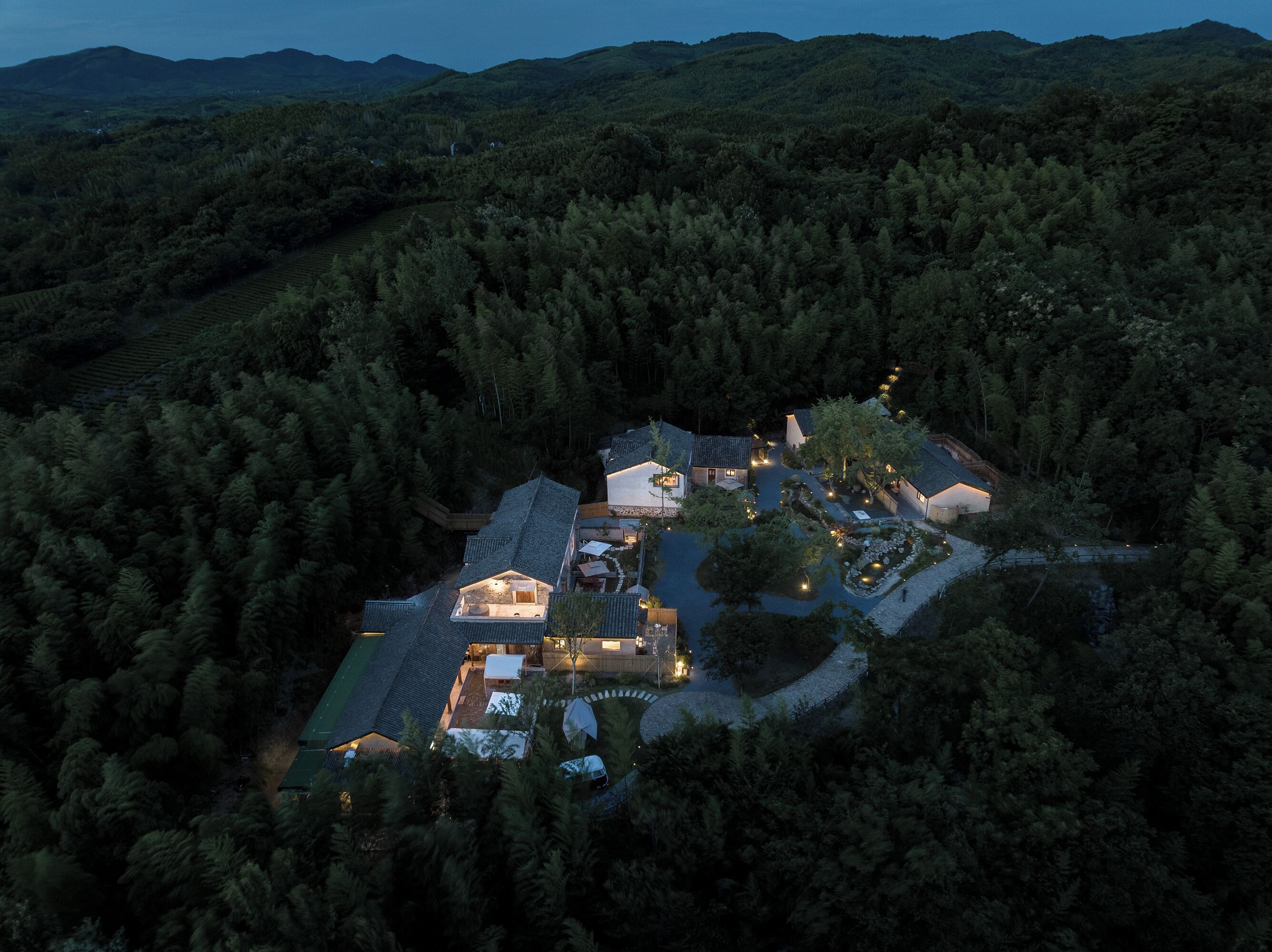 Vista aérea de un resort aislado con varias construcciones, rodeado de un bosque denso, que cuenta con un patio central y un pequeño lago.