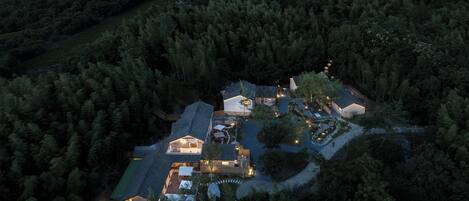 Vista aérea de un resort aislado con varias construcciones, rodeado de un bosque denso, que cuenta con un patio central y un pequeño lago.