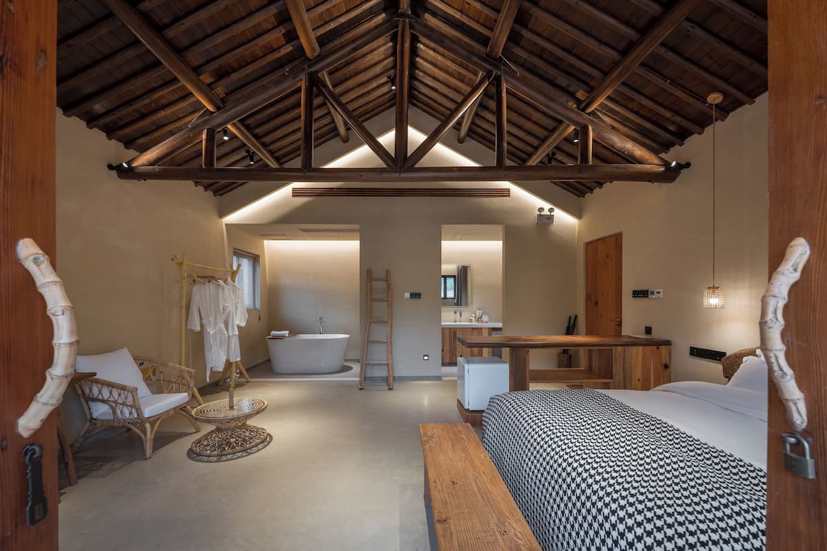 A spacious bedroom with a large bed, a wooden desk, a chair, and a bathtub.
