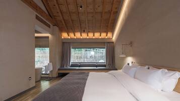 A bedroom with a large bed, a window seat, and a view of greenery outside.