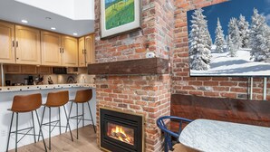 A kitchen with wooden cabinets, a brick fireplace, and a dining area with a marble table and bar stools.
