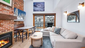 A cozy living room with a fireplace, a sofa, a table, and a view of the outside.