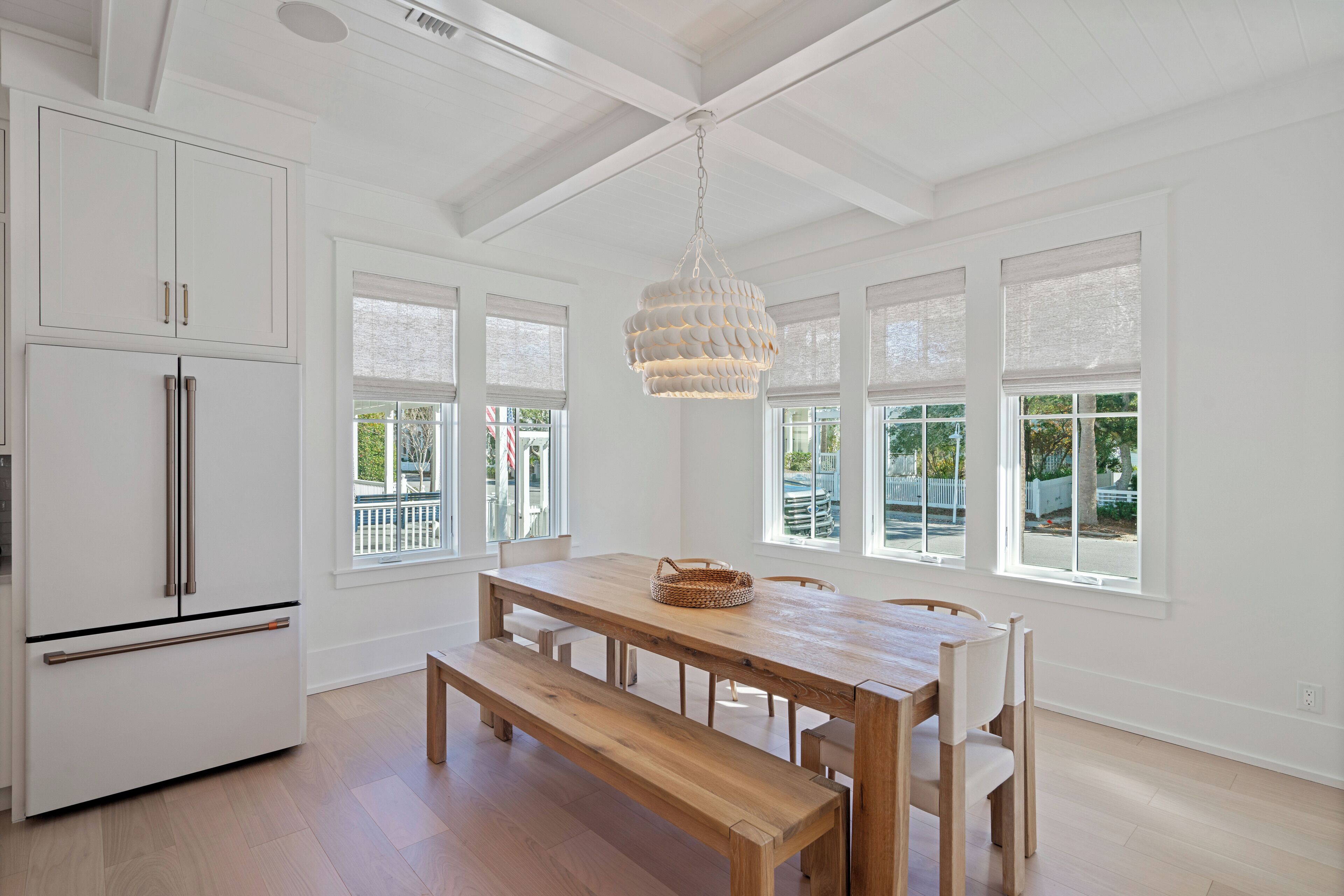 Una cocina con muebles blancos, una mesa de comedor de madera con bancos y una lámpara colgante.