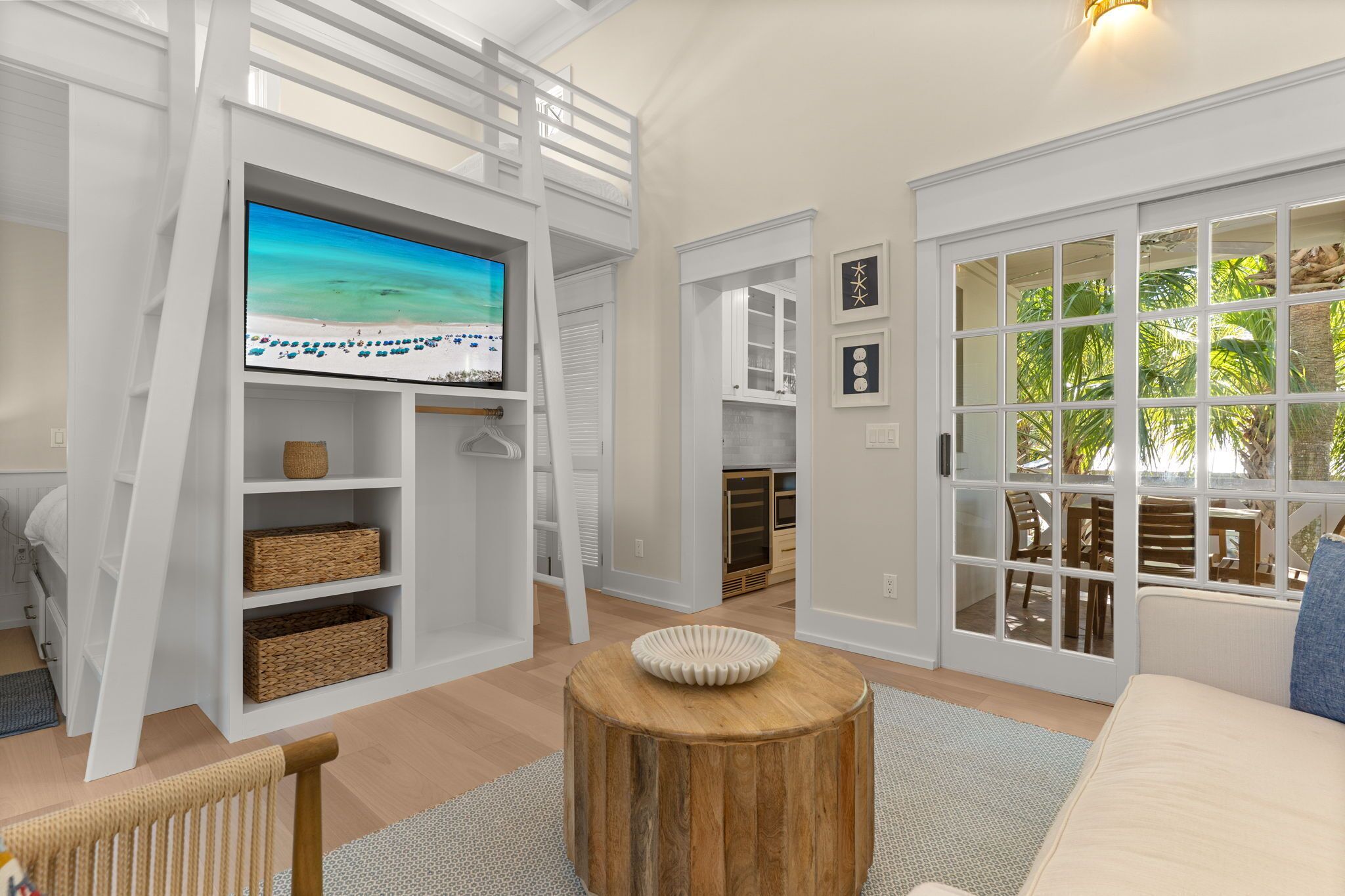 Una sala de estar moderna con una televisión, estanterías de madera, una mesa redonda de madera y vistas a un área exterior a través de puertas de cristal.