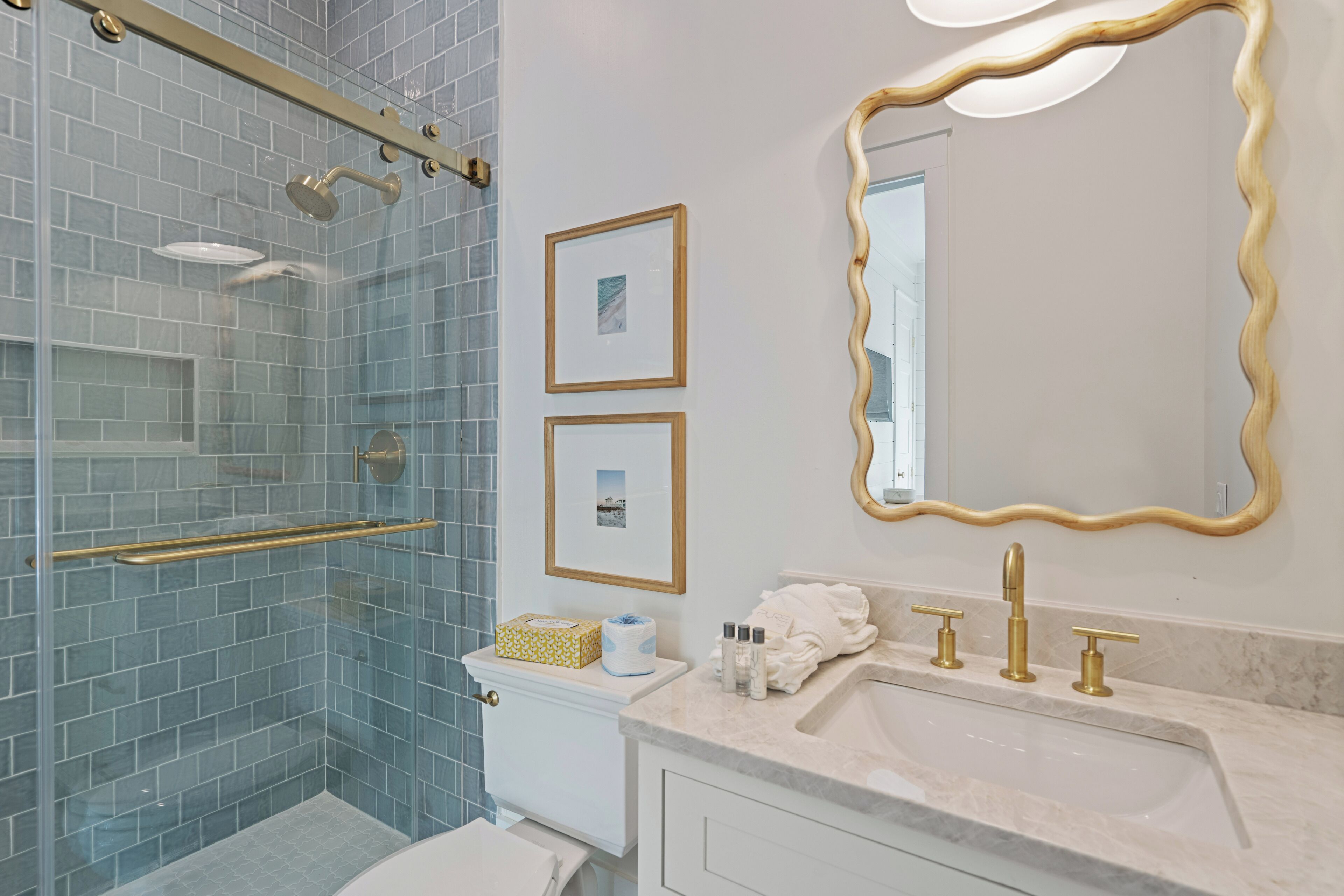 Un bagno con box doccia in vetro, un water bianco, un mobile lavabo con piano in marmo e un grande specchio con cornice ondulata.
