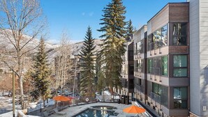 Un bâtiment moderne doté d’un espace piscine, entouré d’arbres et de montagnes.