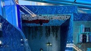 Un grand jacuzzi intérieur, avec un revêtement intérieur en marbre bleu, entouré de murs en pierre et agrémenté d’une composition florale décorative.