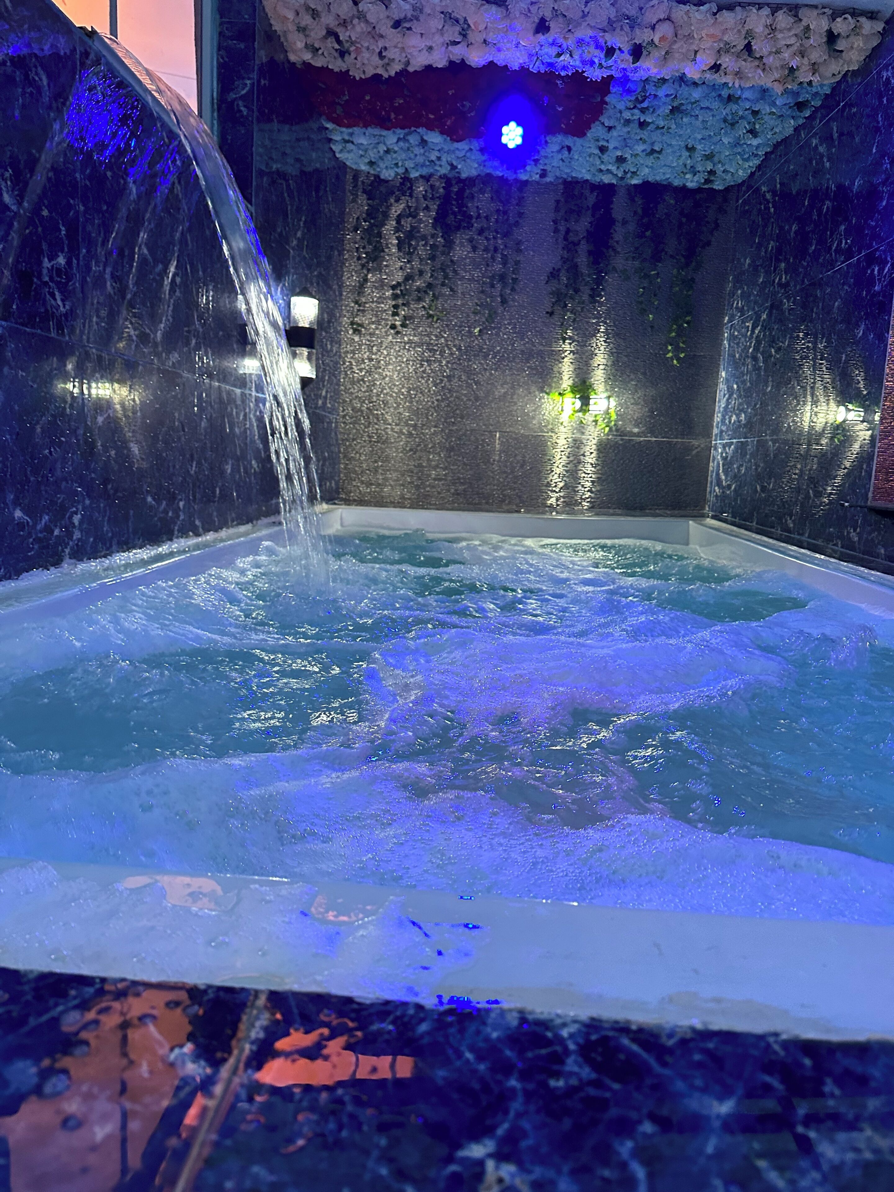 Een whirlpool met waterstralen, omgeven door donker marmeren wanden en bloemendecoraties.