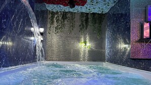 Un bain à remous doté de jets d’eau, entouré d’un mur carrelé agrémenté d’une composition florale.